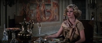 Movie still from “The Spy Who Loved Me” (1977), directed by Lewis Gilbert – A woman sitting at a table with a plate of food on top of it; Medium shot, Over the shoulder angle