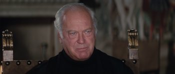 Movie still from “The Spy Who Loved Me” (1977), directed by Lewis Gilbert – An older man wearing a black shirt and looking at the camera; Close Up shot, Over the shoulder angle