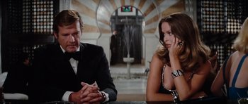 Movie still from “The Spy Who Loved Me” (1977), directed by Lewis Gilbert – A man and a woman sitting at a table in front of an elevator; Medium shot, Over the shoulder angle