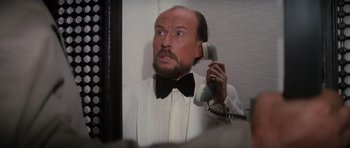 Movie still from “The Spy Who Loved Me” (1977), directed by Lewis Gilbert – A man with a beard is holding up a phone; Close Up shot, Low angle