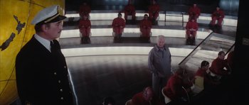 Movie still from “The Spy Who Loved Me” (1977), directed by Lewis Gilbert – A group of men in red suits sitting in a circle; Wide shot, High angle