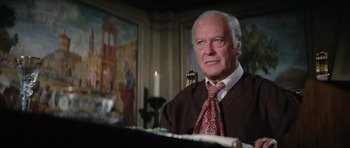 Movie still from “The Spy Who Loved Me” (1977), directed by Lewis Gilbert – An older man wearing a neck tie in front of a painting; Close Up shot, Low angle