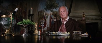 Movie still from “The Spy Who Loved Me” (1977), directed by Lewis Gilbert – An older man sitting at a dinner table; Medium shot, Low angle