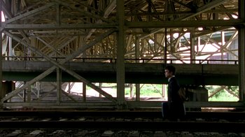 Movie still from “The Station Agent” (2003), directed by Tom McCarthy – A man standing on a train track near a wooden structure; Extreme Wide shot, Low angle