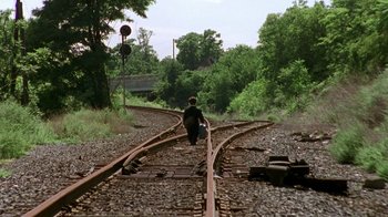 Movie still from “The Station Agent” (2003), directed by Tom McCarthy – A person walking down a train track carrying a bag; Extreme Wide shot, High angle