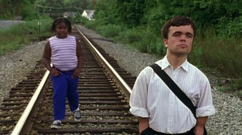 Movie still from “The Station Agent” (2003), directed by Tom McCarthy – A man and a girl are standing on the railroad tracks; Medium shot, Low angle