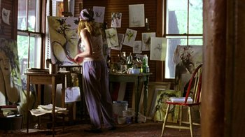 Movie still from “The Station Agent” (2003), directed by Tom McCarthy – A woman standing in front of an easel in a room filled with paintings; Wide shot, Low angle