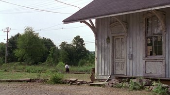 Movie still from “The Station Agent” (2003), directed by Tom McCarthy – A person walking in front of an old train station; Extreme Wide shot, Low angle