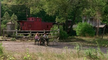 Movie still from “The Station Agent” (2003), directed by Tom McCarthy – Two people sitting at a table near a red train car; Extreme Wide shot, High angle