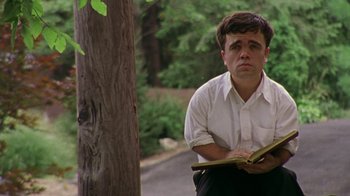 Movie still from “The Station Agent” (2003), directed by Tom McCarthy – A man sitting on the side of the road holding a book; Medium shot, Low angle
