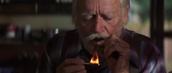 Movie still from “The Straight Story” (1999), directed by David Lynch – An older man lighting a match with a cigarette in his mouth; Close Up shot, Low angle