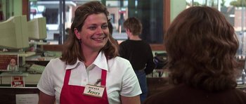 Movie still from “The Straight Story” (1999), directed by David Lynch – A woman wearing an apron smiles at the camera; Medium shot, Over the shoulder angle