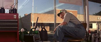 Movie still from “The Straight Story” (1999), directed by David Lynch – An older man sitting in front of a store window; Medium shot, Low angle
