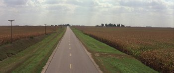 Movie still from “The Straight Story” (1999), directed by David Lynch – An empty road in the middle of an open field; Extreme Wide shot, High angle