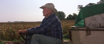 Movie still from “The Straight Story” (1999), directed by David Lynch – An older man wearing a cowboy hat sitting on the back of a tractor; Medium shot, Low angle