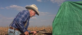 Movie still from “The Straight Story” (1999), directed by David Lynch – An older man in a cowboy hat is looking at a tent; Medium shot, Over the shoulder angle
