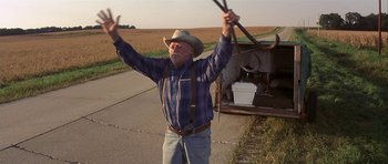 Movie still from “The Straight Story” (1999), directed by David Lynch – An older man holding a stick near an overturned car; Medium shot, Low angle