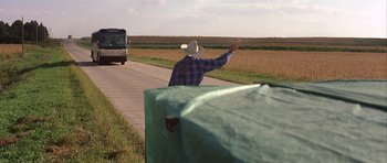 Movie still from “The Straight Story” (1999), directed by David Lynch – A man in a cowboy hat waves at a bus; Extreme Wide shot, Over the shoulder angle