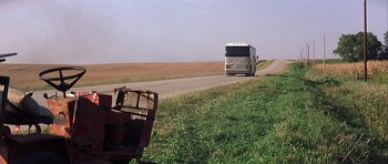 Movie still from “The Straight Story” (1999), directed by David Lynch – A bus driving down a road next to a field; Extreme Wide shot, High angle