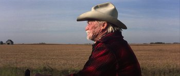 Movie still from “The Straight Story” (1999), directed by David Lynch – An older man wearing a cowboy hat in the middle of a field; Close Up shot, Over the shoulder angle