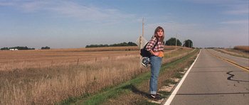 Movie still from “The Straight Story” (1999), directed by David Lynch – A woman standing on the side of a road holding a bag; Wide shot, Low angle