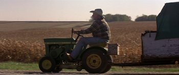 Movie still from “The Straight Story” (1999), directed by David Lynch – An older man riding a tractor on a dirt road; Wide shot, High angle