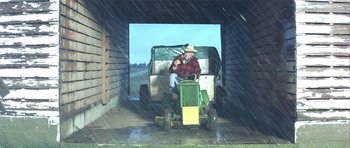 Movie still from “The Straight Story” (1999), directed by David Lynch – An older man riding a tractor in the rain; Wide shot, High angle