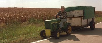 Movie still from “The Straight Story” (1999), directed by David Lynch – An older man riding a tractor down a road; Wide shot, Low angle