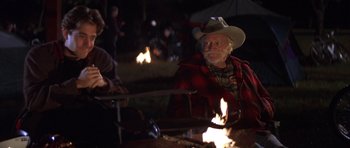 Movie still from “The Straight Story” (1999), directed by David Lynch – An old man wearing a cowboy hat sitting next to a fire; Medium shot, Over the shoulder angle