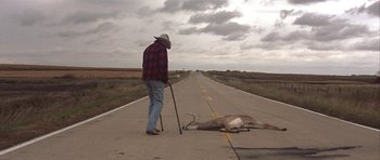 Movie still from “The Straight Story” (1999), directed by David Lynch – A man standing on the side of a road next to a dead animal; Wide shot, High angle