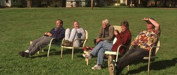Movie still from “The Straight Story” (1999), directed by David Lynch – A group of people sitting in lawn chairs on the grass; Wide shot, High angle