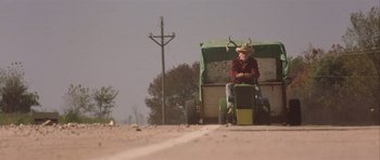 Movie still from “The Straight Story” (1999), directed by David Lynch – An old man sitting on top of a green tractor; Wide shot, Low angle