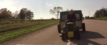 Movie still from “The Straight Story” (1999), directed by David Lynch – An older man riding a tractor down a road; Wide shot, Low angle