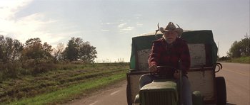 Movie still from “The Straight Story” (1999), directed by David Lynch – An older man driving a tractor down a road; Medium shot, Low angle