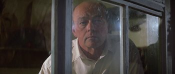 Movie still from “The Straight Story” (1999), directed by David Lynch – A bald man looking out of a window at the camera; Close Up shot, Low angle