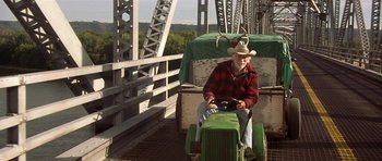 Movie still from “The Straight Story” (1999), directed by David Lynch – An older man riding a toy tractor across a bridge; Wide shot, Low angle