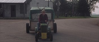 Movie still from “The Straight Story” (1999), directed by David Lynch – An older man riding a tractor on the street; Wide shot, High angle