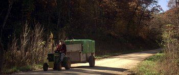 Movie still from “The Straight Story” (1999), directed by David Lynch – An older man riding a tractor with a trailer; Wide shot, High angle