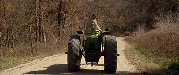 Movie still from “The Straight Story” (1999), directed by David Lynch – A man riding a tractor down a dirt road; Wide shot, Low angle
