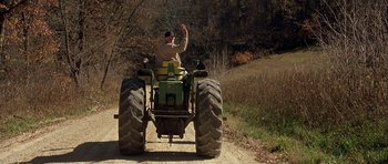 Movie still from “The Straight Story” (1999), directed by David Lynch – A man riding a tractor down a dirt road; Wide shot, High angle