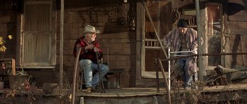 Movie still from “The Straight Story” (1999), directed by David Lynch – An old man sitting on a chair in front of a building; Wide shot, Low angle