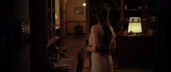 Movie still from “The Strangers” (2008), directed by Bryan Bertino – A woman in a white dress standing in front of a chair; Wide shot, Over the shoulder angle