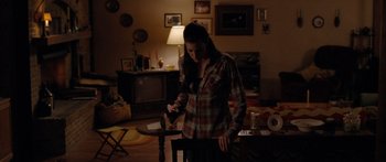 Movie still from “The Strangers” (2008), directed by Bryan Bertino – A woman standing in a living room holding a wine bottle; Medium shot, High angle