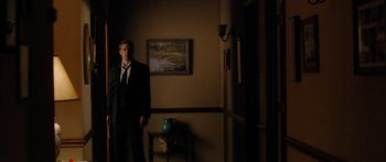 Movie still from “The Strangers” (2008), directed by Bryan Bertino – A man standing in a dark room next to a painting; Wide shot, Low angle