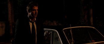 Movie still from “The Strangers” (2008), directed by Bryan Bertino – A man standing next to a car in the dark at night; Medium shot, Over the shoulder angle