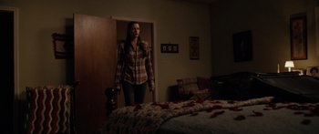 Movie still from “The Strangers” (2008), directed by Bryan Bertino – A woman standing in front of a bed in a room; Wide shot, Over the shoulder angle