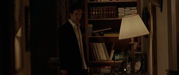 Movie still from “The Strangers” (2008), directed by Bryan Bertino – A man in a suit standing in front of a book case; Medium shot, Over the shoulder angle