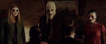 Movie still from “The Strangers” (2008), directed by Bryan Bertino – A man wearing a white mask standing in front of a group of people; Medium shot, Over the shoulder angle