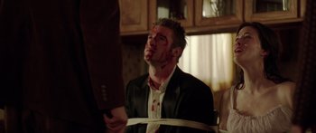 Movie still from “The Strangers” (2008), directed by Bryan Bertino – A man with blood on his face tied to a chair; Medium shot, Over the shoulder angle