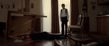 Movie still from “The Strangers” (2008), directed by Bryan Bertino – A young man standing in a living room next to a dead body; Wide shot, High angle